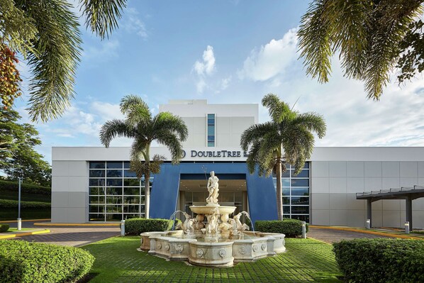 A Doubletree hotel with a fountain, palm trees, and a clear blue sky.