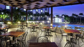 An outdoor dining area with tables and chairs, overlooking a swimming pool and a building with large windows. - DoubleTree by Hilton Managua (Managua)
