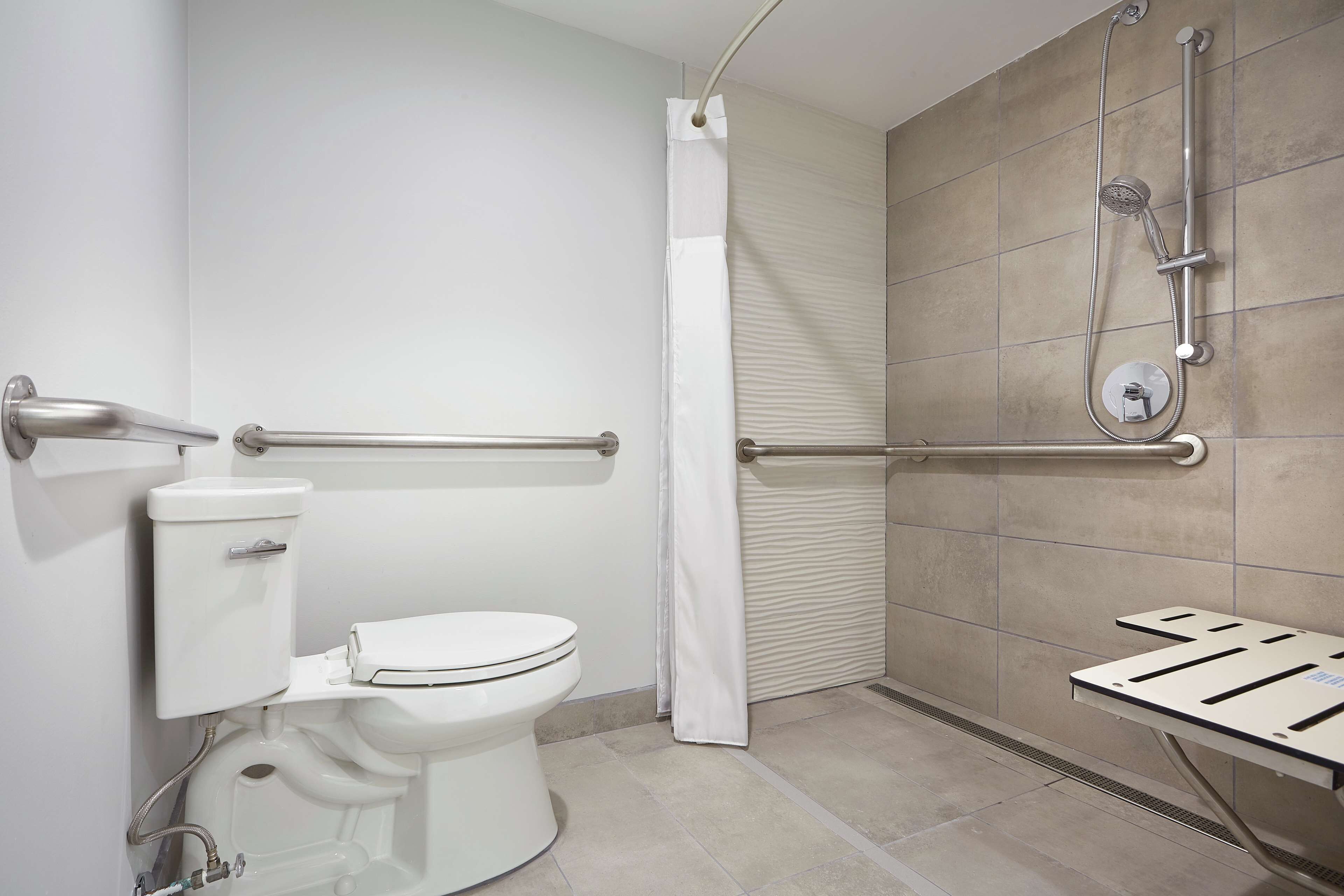 A modern bathroom with a toilet, shower, and grab bar.