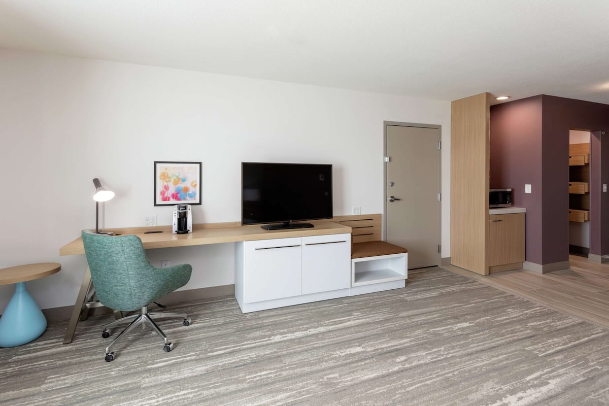 A modern room with a wooden desk, a television, a teal office chair, and a small side table.