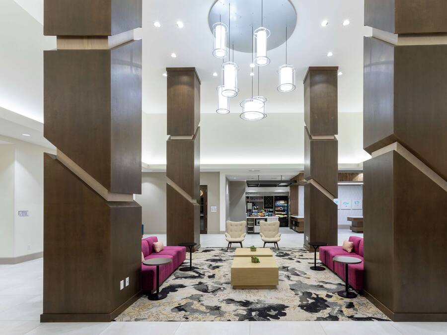 Un lobby moderno con una zona de estar central, una escalera y una cocina al fondo.