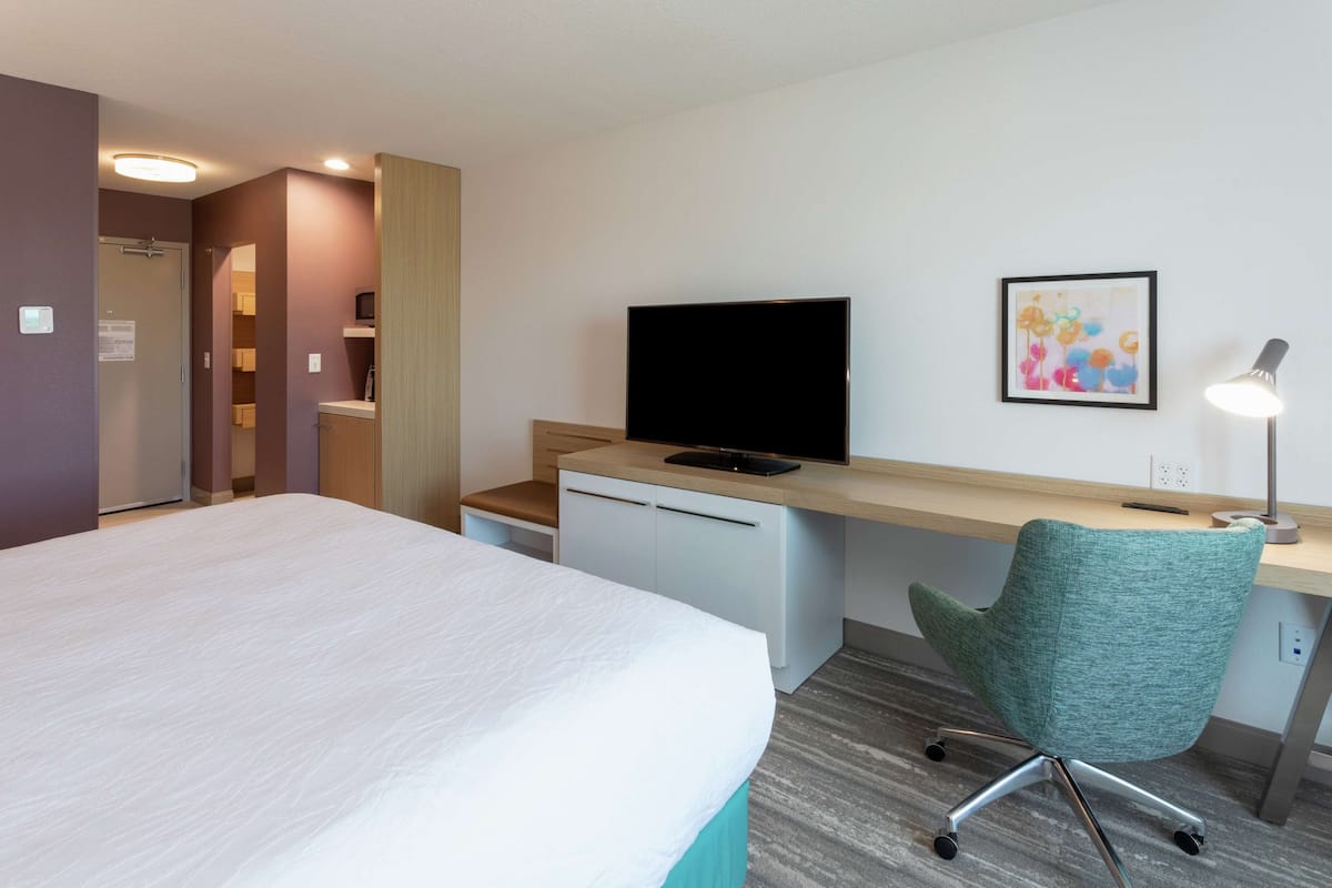 A hotel room with a bed, a desk with a computer, a TV, and a chair.