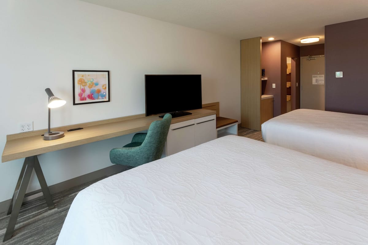 A hotel room with a desk, a television, a bed, and a bathroom.