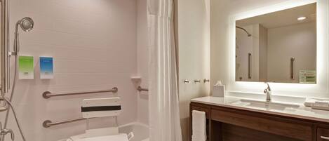 A modern bathroom with a walk-in shower, grab bars, a vanity with a mirror, and a toilet with a safety seat.