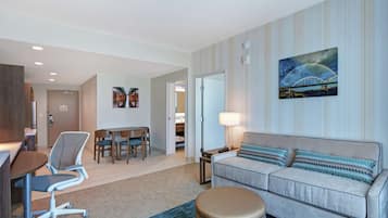 Habitación de hotel con sofá, escritorio, silla, lámpara y un cuadro de un puente.
