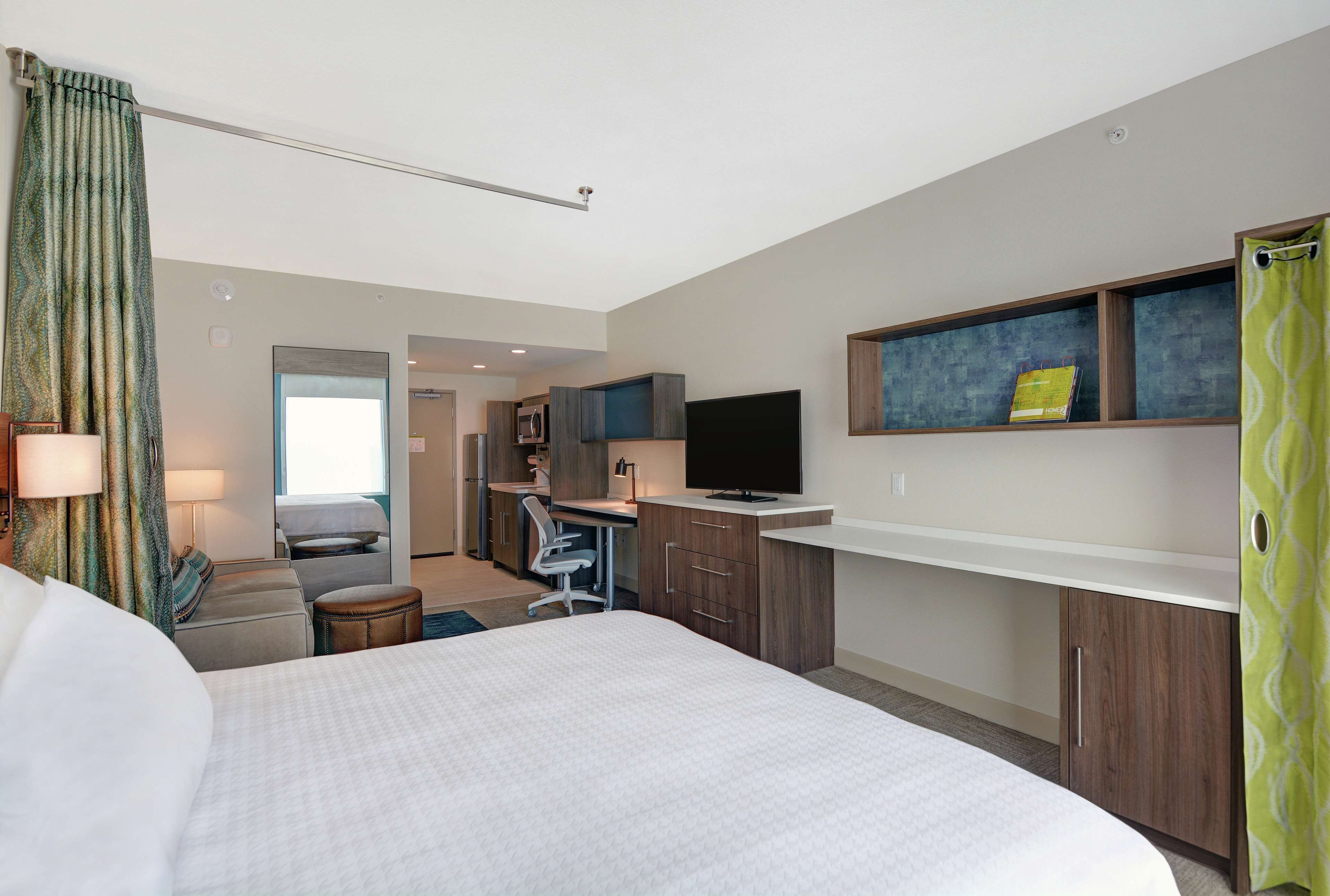 Une chambre d’hôtel avec un grand lit, un bureau avec un ordinateur, une télévision et une petite kitchenette.