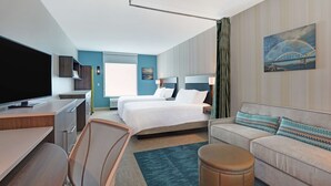 Une chambre d’hôtel moderne dotée d’un grand lit, d’un bureau avec un téléviseur à écran plat, d’un canapé et d’un petit pouf.