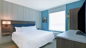 Habitación de hotel con una cama grande, un escritorio con computadora, un televisor, una ventana con vista y un cuadro en la pared.