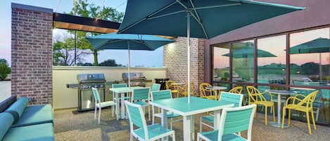 An outdoor patio with tables and chairs, a grill, and umbrellas.