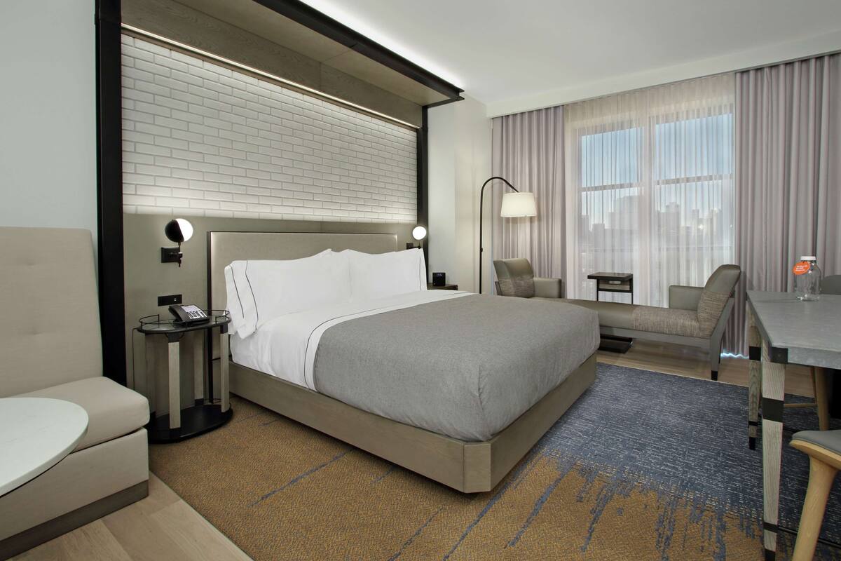A modern hotel room with a large bed, a desk, a chair, and a sofa.