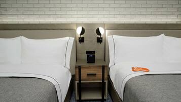 Habitación de hotel con dos camas, una mesita de noche de madera con un reloj digital y dos lámparas fijadas a la pared.