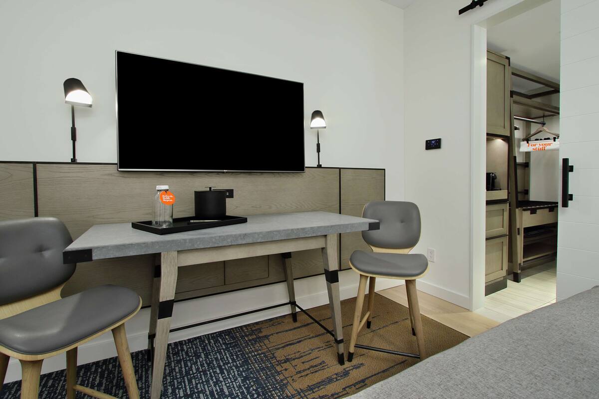 A modern hotel room with a flat-screen TV, two bedside lamps, a small table with a bottle, and a chair.