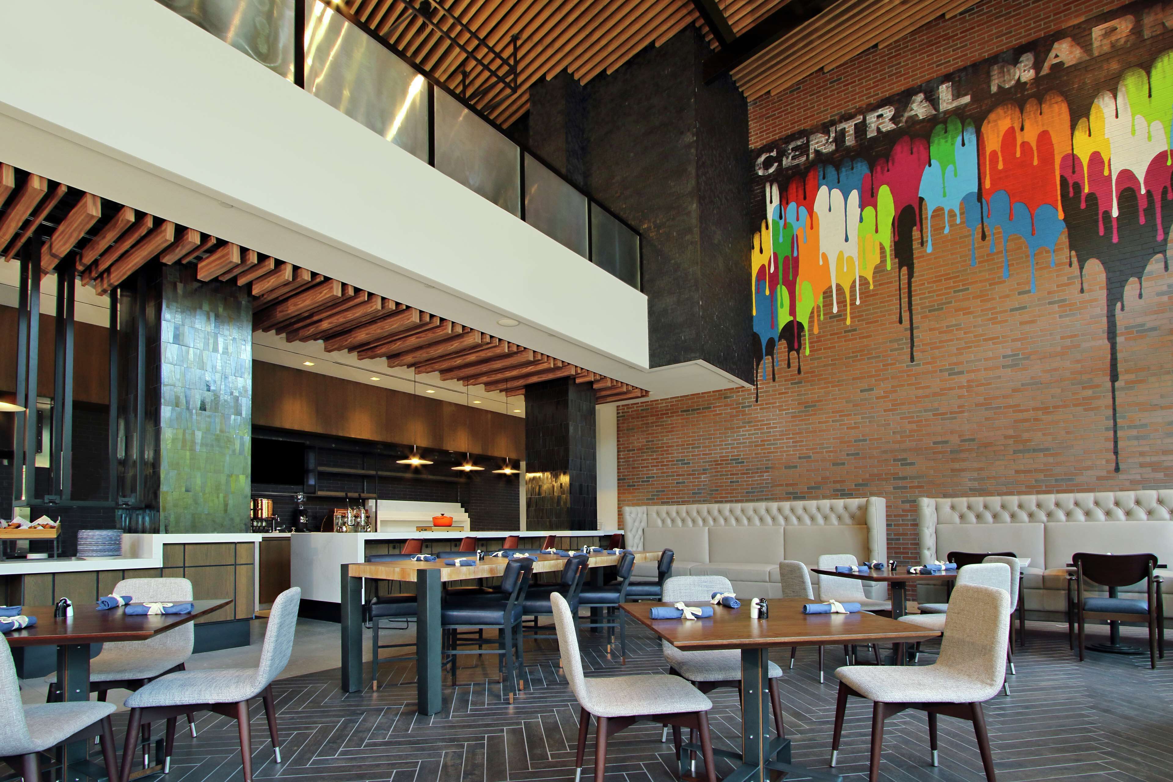 A modern restaurant with a high ceiling, exposed wooden beams, and a colorful mural on the wall.