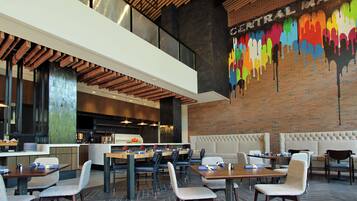 A modern restaurant with a high ceiling, exposed wooden beams, and a colorful mural on the wall.