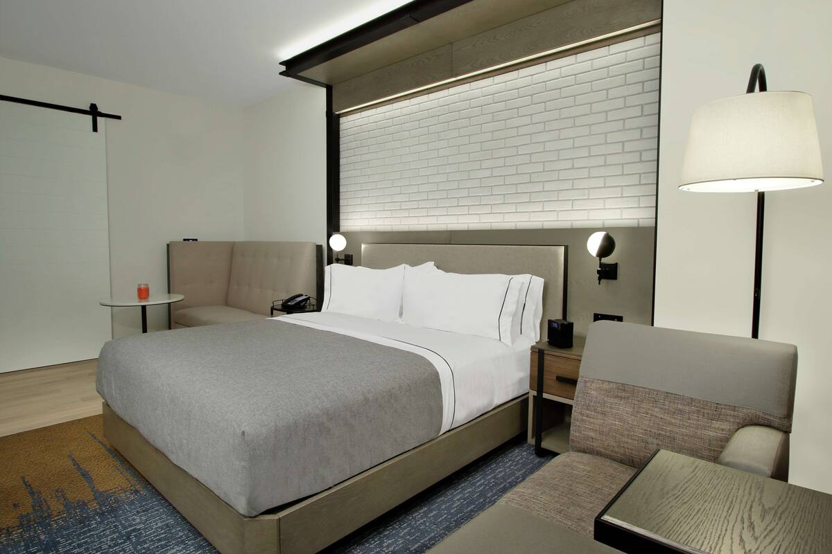 A modern hotel room with a large bed, bedside tables, a lamp, and a seating area.