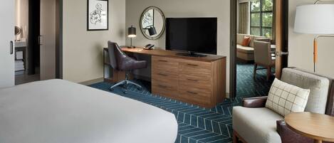 Un cuarto de hotel con una cama grande, un escritorio con computadora, un televisor, una silla, una mesita y vista al exterior.