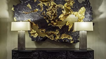 Ein modernes Interieur mit einem großen, schwarz-goldenen abstrakten Wandbild über einem schwarzen Konsolentisch mit zwei Lampen.