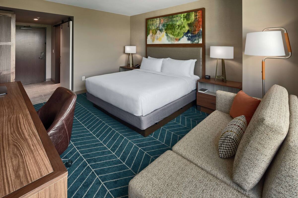 Een hotelkamer met een groot bed, een bureau, een slaapbank en twee bedlampjes.