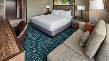 Una habitación de hotel con una cama grande, un escritorio, un sofá y dos lámparas de noche.