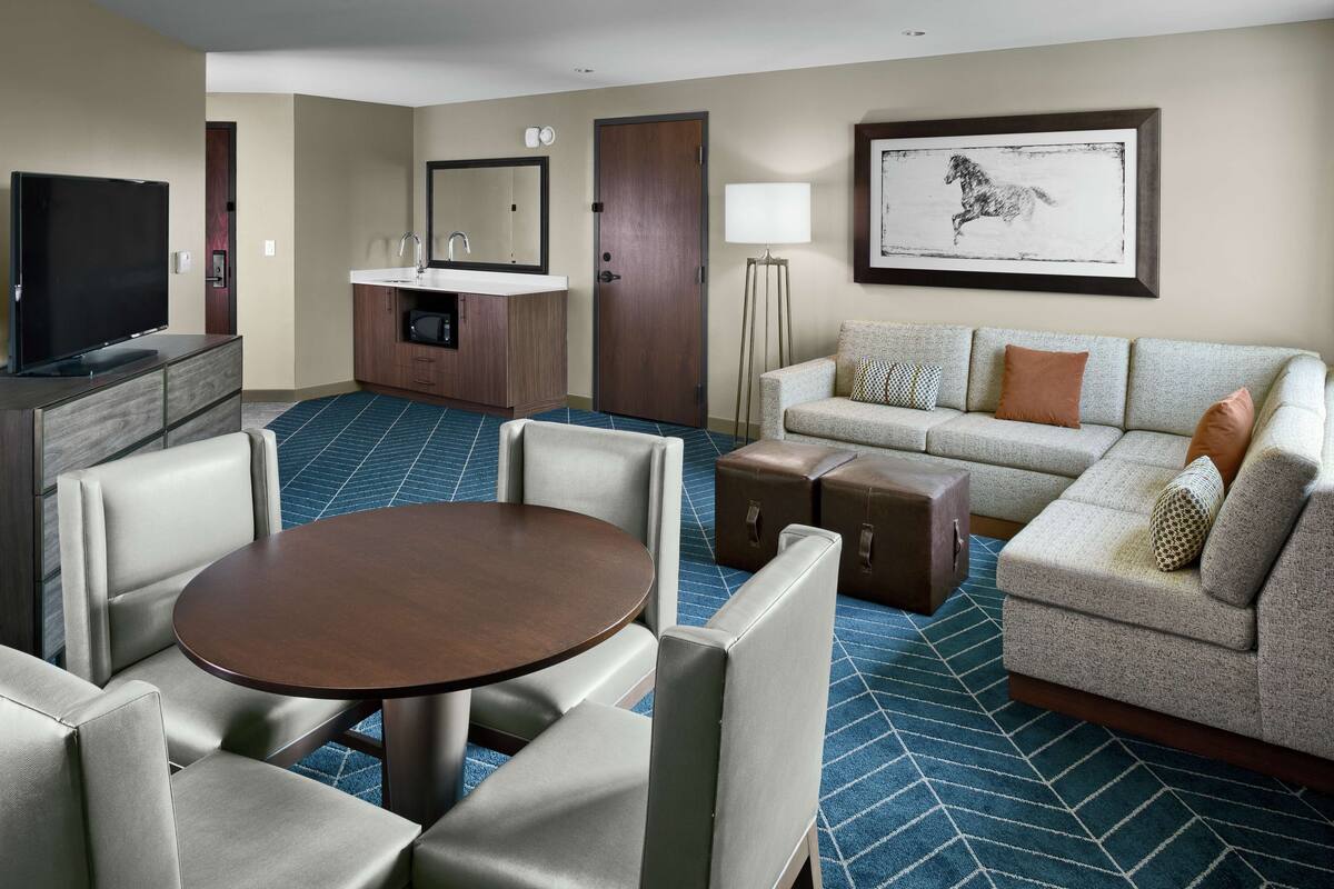 Een hotelkamer met een flatscreen televisie, een bank, een eettafel en een kleine kitchenette.