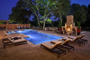 Un área de piscina al aire libre con sillones de descanso y una chimenea de piedra.