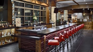 Un espace bar doté d’un long comptoir, de tabourets de bar rouges et d’une variété de bouteilles et de verres.