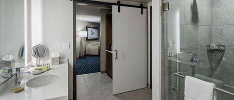 Un baño moderno con cabina de ducha de vidrio, un lavabo blanco con espejo y una puerta que da a un dormitorio.