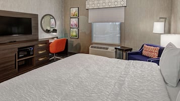 A hotel room with a large bed, a TV, a desk, a chair, and a window with a view.