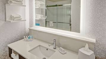 Un baño moderno con un espejo grande, un lavamanos con grifo y repisas con toallas dobladas.