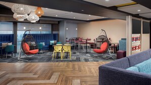 A modern lounge area with seating options including hanging chairs and sofas, a herringbone-patterned floor, and a variety of tables and chairs. - Tru by Hilton Rapid City Rushmore (Rapid City)