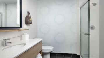 Un baño moderno con cabina de ducha de vidrio, inodoro blanco y tocador con espejo y lavabo.