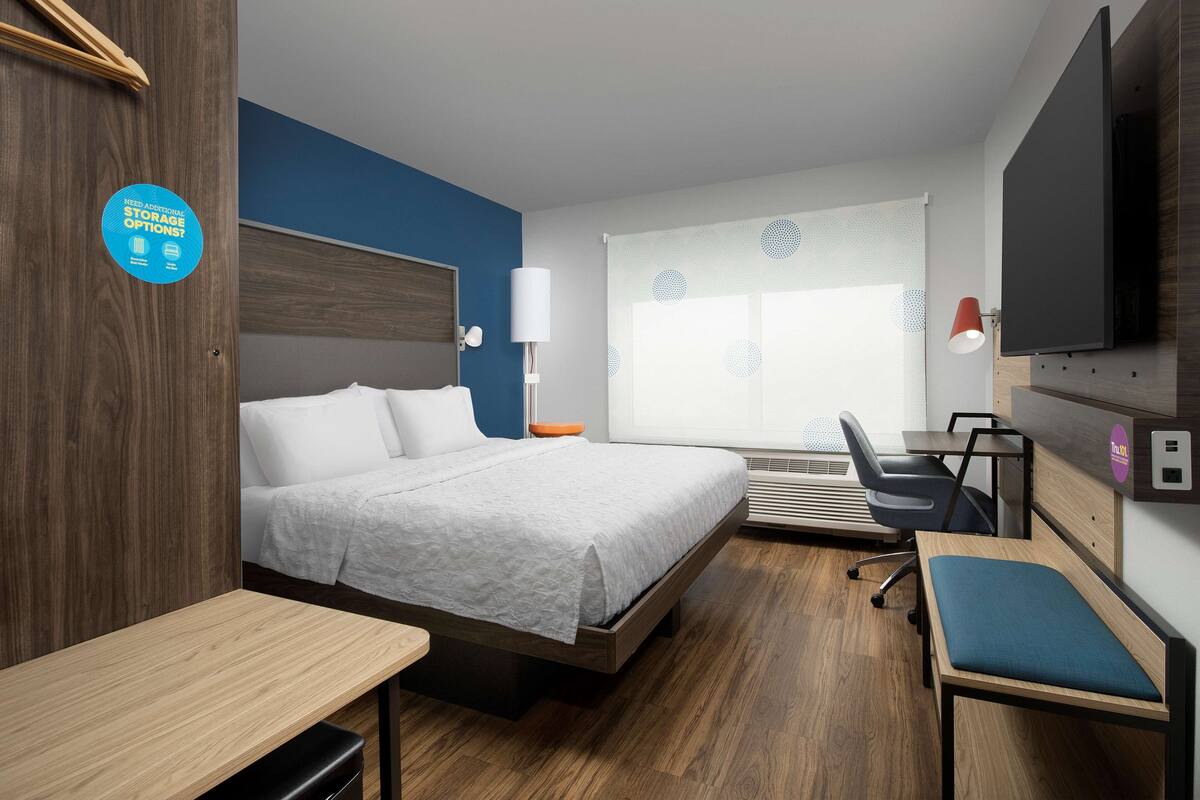 Une chambre d’hôtel équipée d’un lit, d’un bureau, d’une chaise et d’un téléviseur fixé au mur.