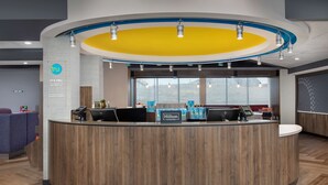 A modern hotel reception area with a wooden reception desk, a large window offering a view, and a sign indicating it's a Hilton hotel. - Tru by Hilton Rapid City Rushmore (Rapid City)