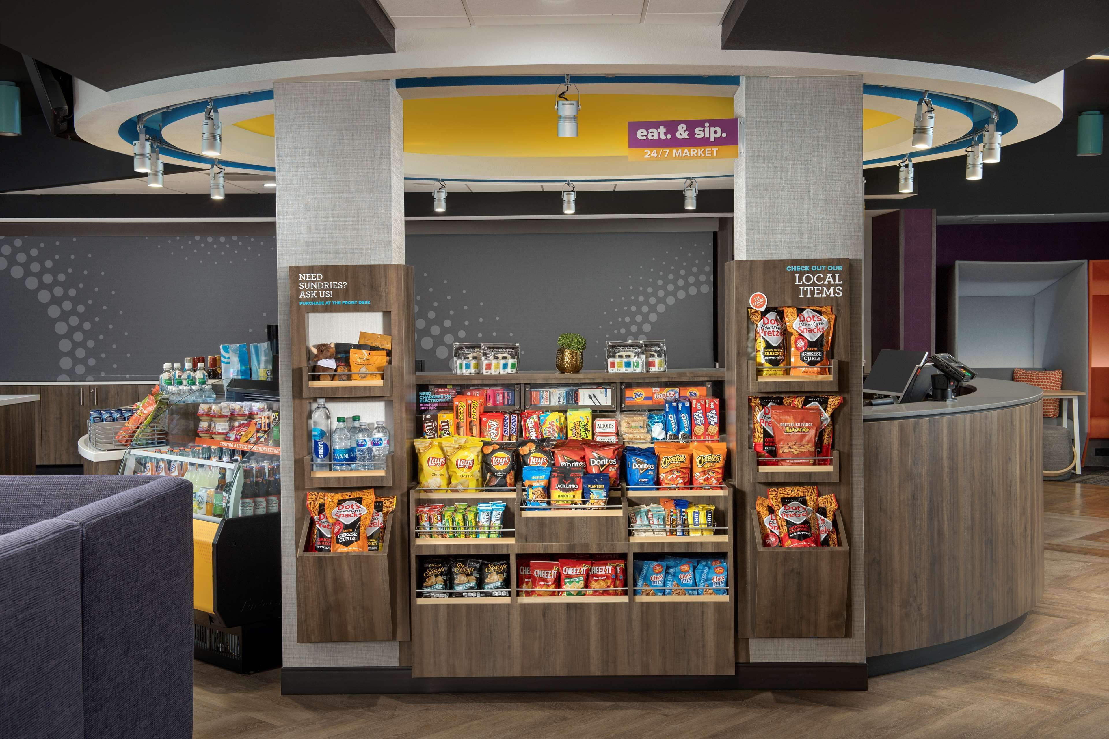 A snack kiosk with a variety of chips and snacks, a beverage section, and a sign advertising a 24/7 market.