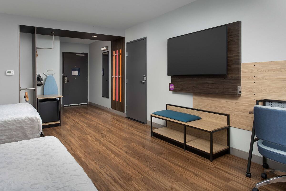 Une chambre d’hôtel moderne équipée de deux lits, d’un bureau, d’une chaise, d’une télévision et d’une armoire.