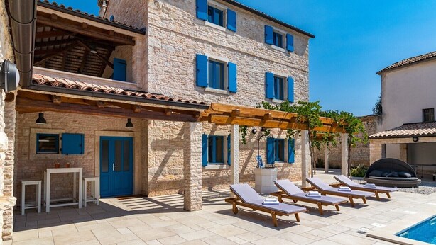 A stone building with a pool area, including lounge chairs and a pergola.