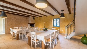 A dining area with a long table set for multiple people, wooden beams on the ceiling, and a staircase to the right.
