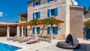 A stone building with a pool, sun loungers, and a covered seating area.