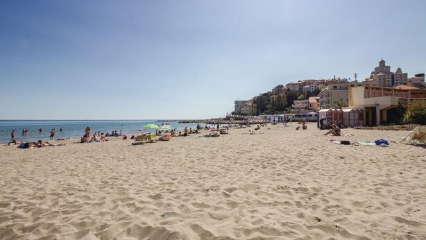 A sandy beach with people sunbathing and swimming, buildings in the background, and a clear sky. - 3 bedroom beautiful home in Imperia -IM- (Imperia -IM-)