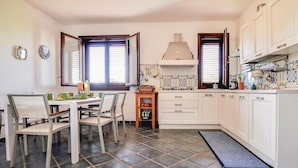 Une cuisine avec des meubles blancs, une table à manger avec des chaises et un sol carrelé.