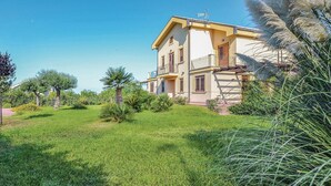 Une maison à deux étages dotée d’un balcon, entourée d’une pelouse bien entretenue et de diverses plantes.