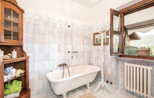 A bathroom with a freestanding bathtub, a wooden cabinet with glass doors, and a window with a view of the outdoors. - Amazing home in Montebuono (Montebuono)