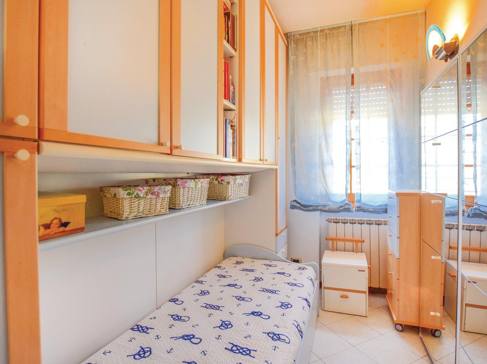 Een kleine slaapkamer met een enkel bed, een houten garderobe, een radiator en een raam met gordijnen.