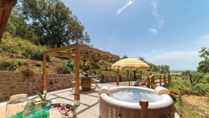 Un jacuzzi con una pérgola de madera y una sombrilla, rodeado de muros de piedra y vegetación.
