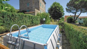 Ein rechteckiger Pool mit integrierter Leiter, umgeben von gepflegten Hecken und einem Steinhaus im Hintergrund.