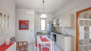 A compact kitchen with white cabinets, a dining area with a red table and chairs, and a small refrigerator.