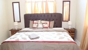A neatly made bed with a patterned bedspread, two bedside tables with lamps, and two wall mirrors. - Your Holiday Home Caribbean Estates (Portmore)