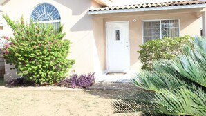A house with a white door, a window with a decorative design, and a small porch area. - Your Holiday Home Caribbean Estates (Portmore)
