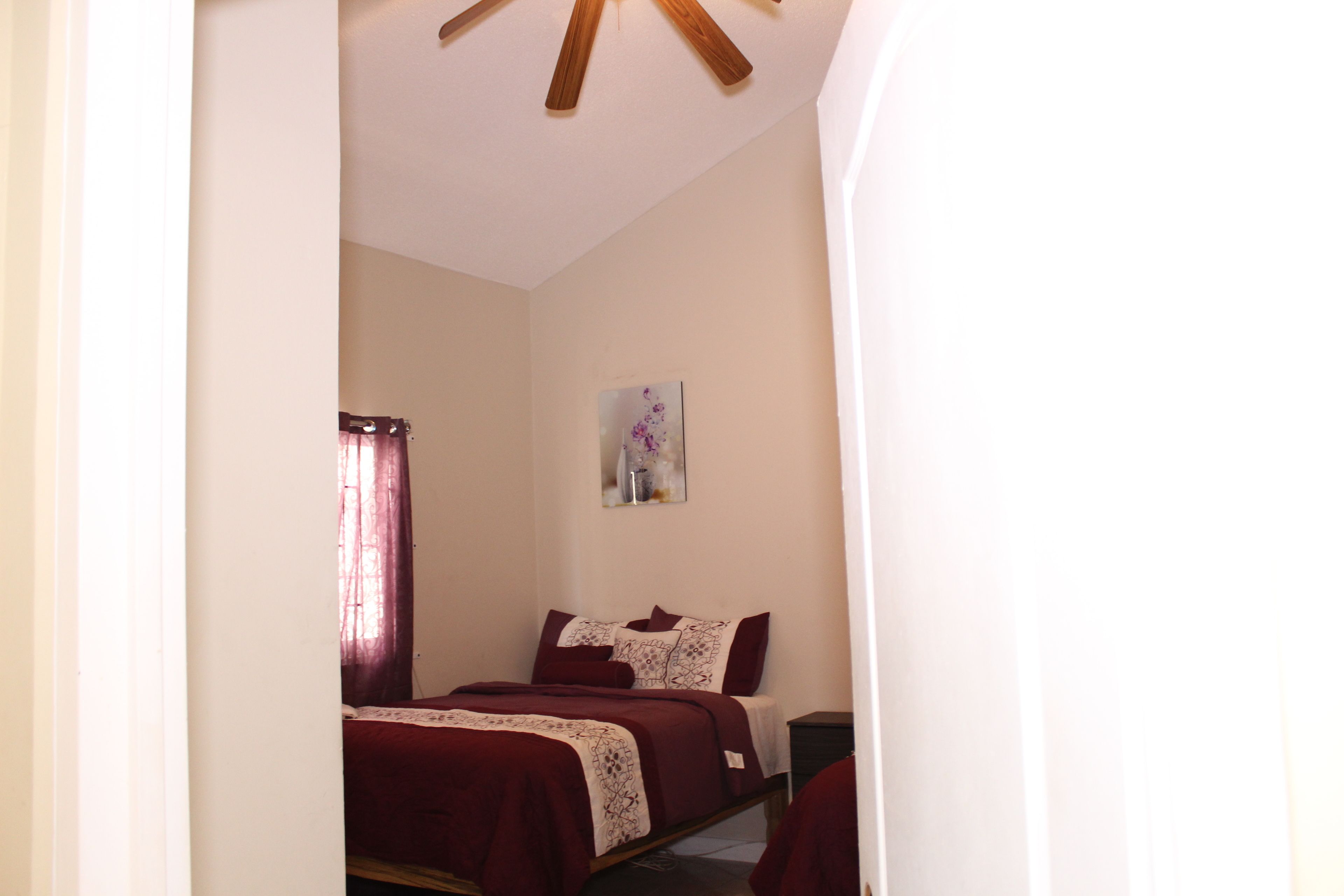 A bedroom with a bed, a nightstand, a painting on the wall, and a ceiling fan.