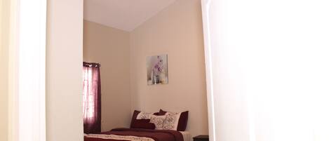 A bedroom with a bed, a nightstand, a painting on the wall, and a ceiling fan.